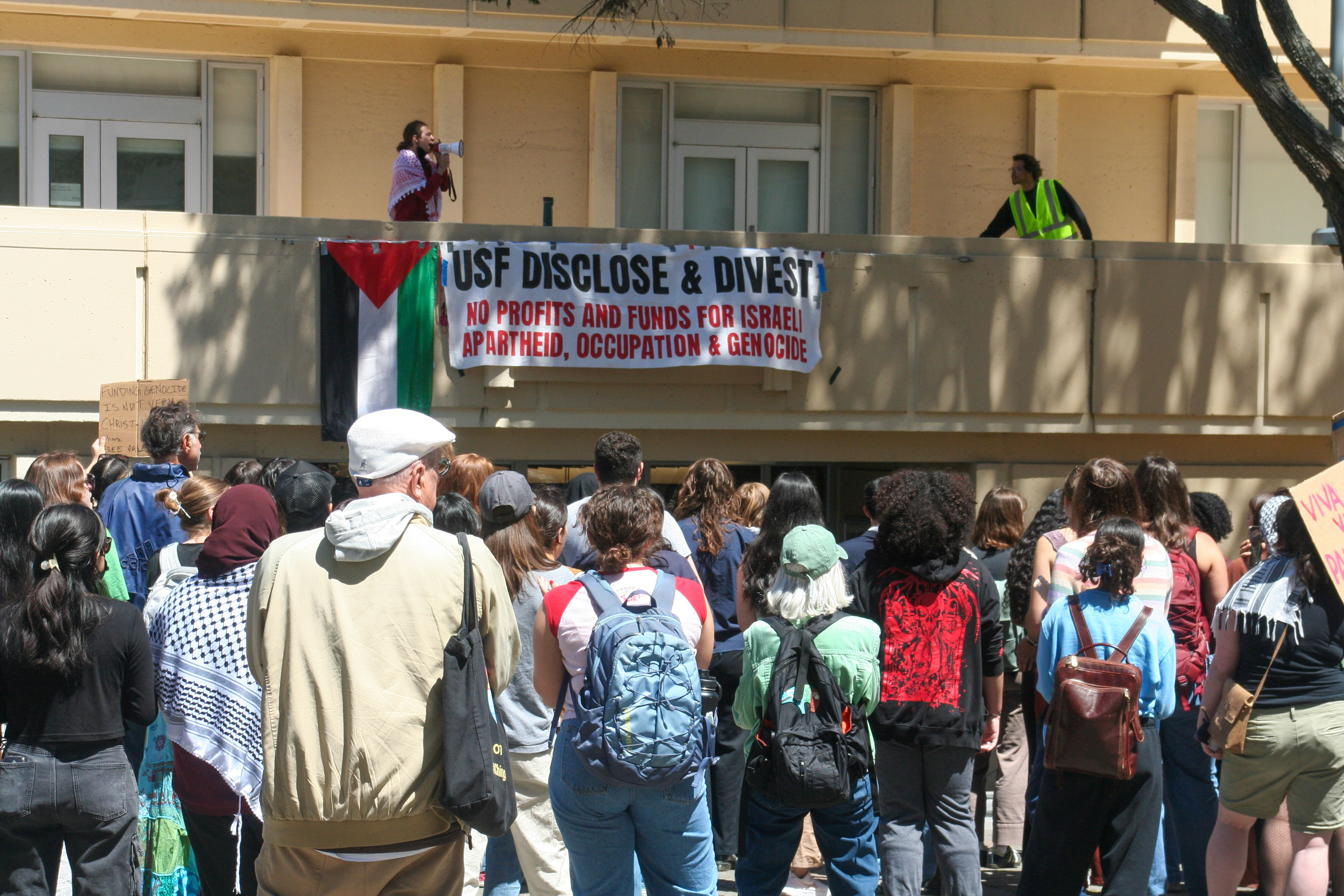 a crowd of protesters, carrying signs and many wearing kufiya