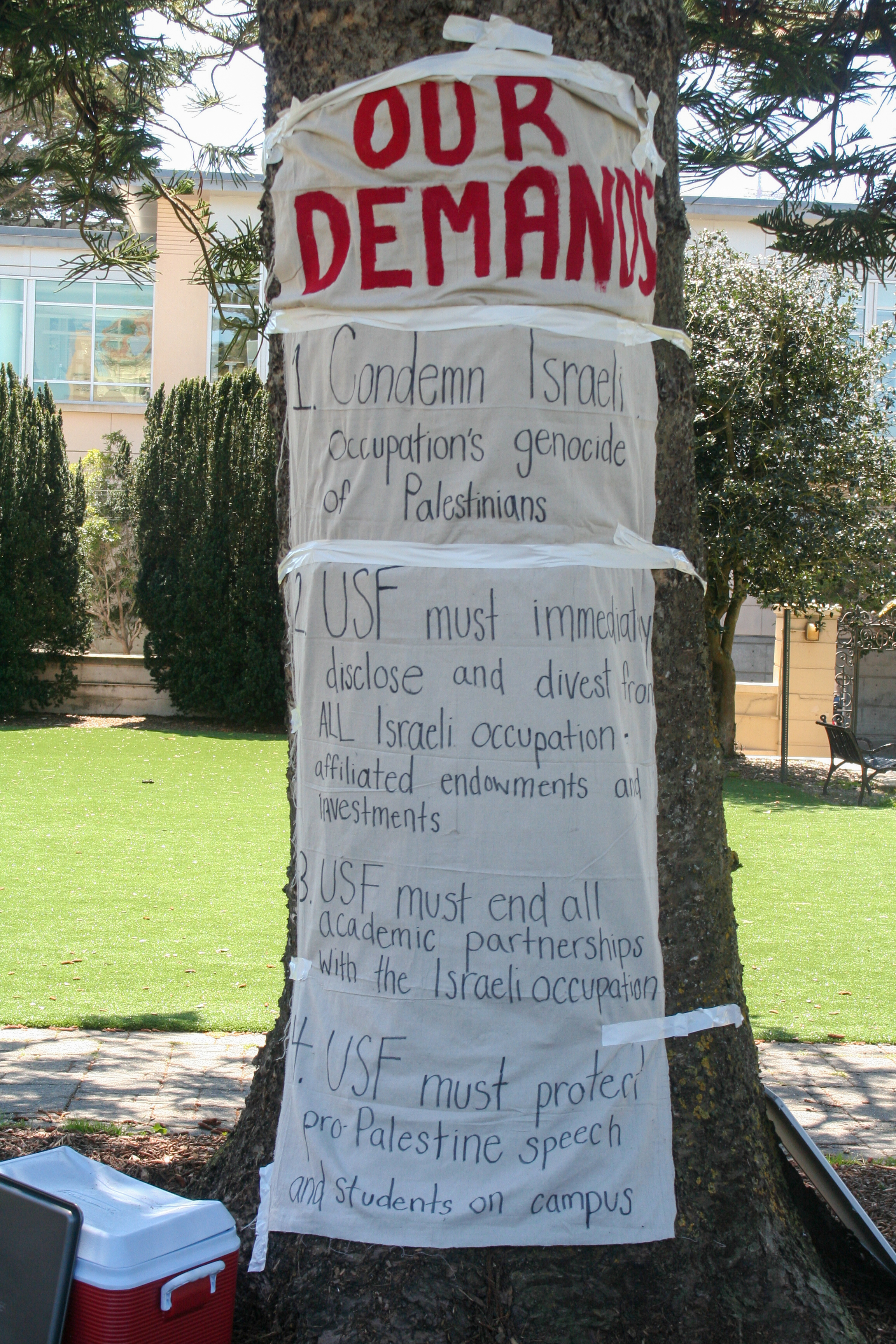 a sign reading: 1. Condemn Israeli occupation’s genocide of Palestinians 2. USF must immediately disclose and divest from all Israeli occupation affiliated endowments and investments 3. USF must end all academic partnerships with the Israeli occupation 4. USF must protect pro-Palestine speach and students on campus